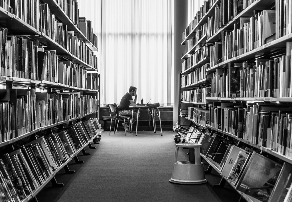 Man sitting studying in a library at the end of two rows of books.
